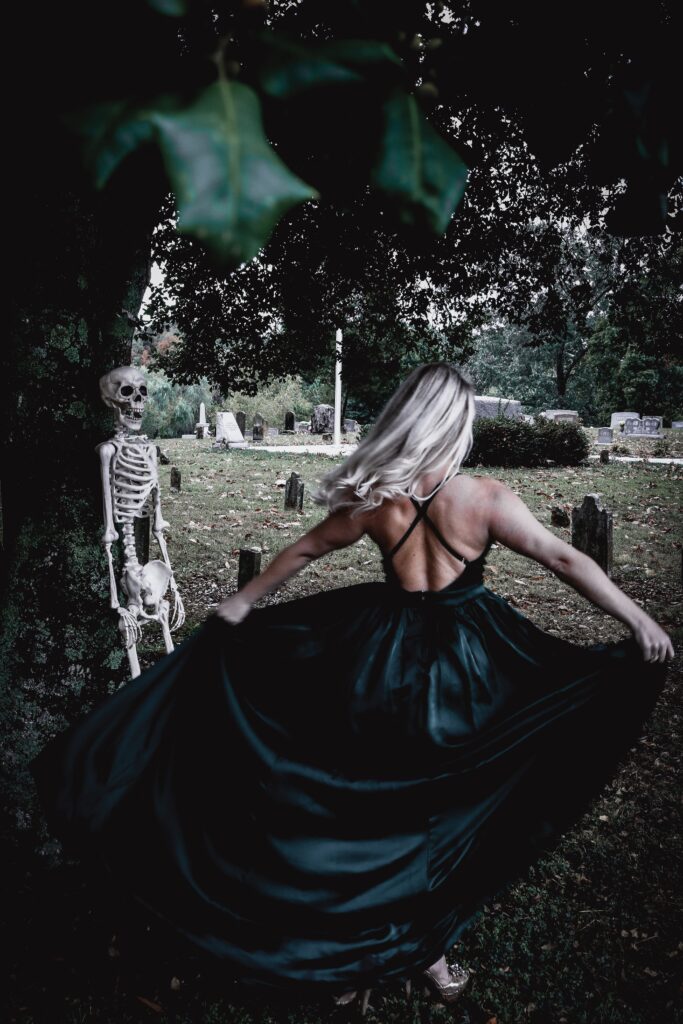Photograph of Stephanie Carroll twirling in a graveyard with a skeleton during spooky season.